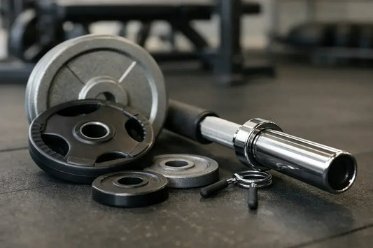 Silver and black weight plates with a chrome finished barbell resting beside them for fitting the bar discussion.