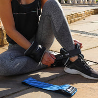 Person sitting on a stone surface wearing gray leggings and black athletic shoes, with ankle weight on one foot.