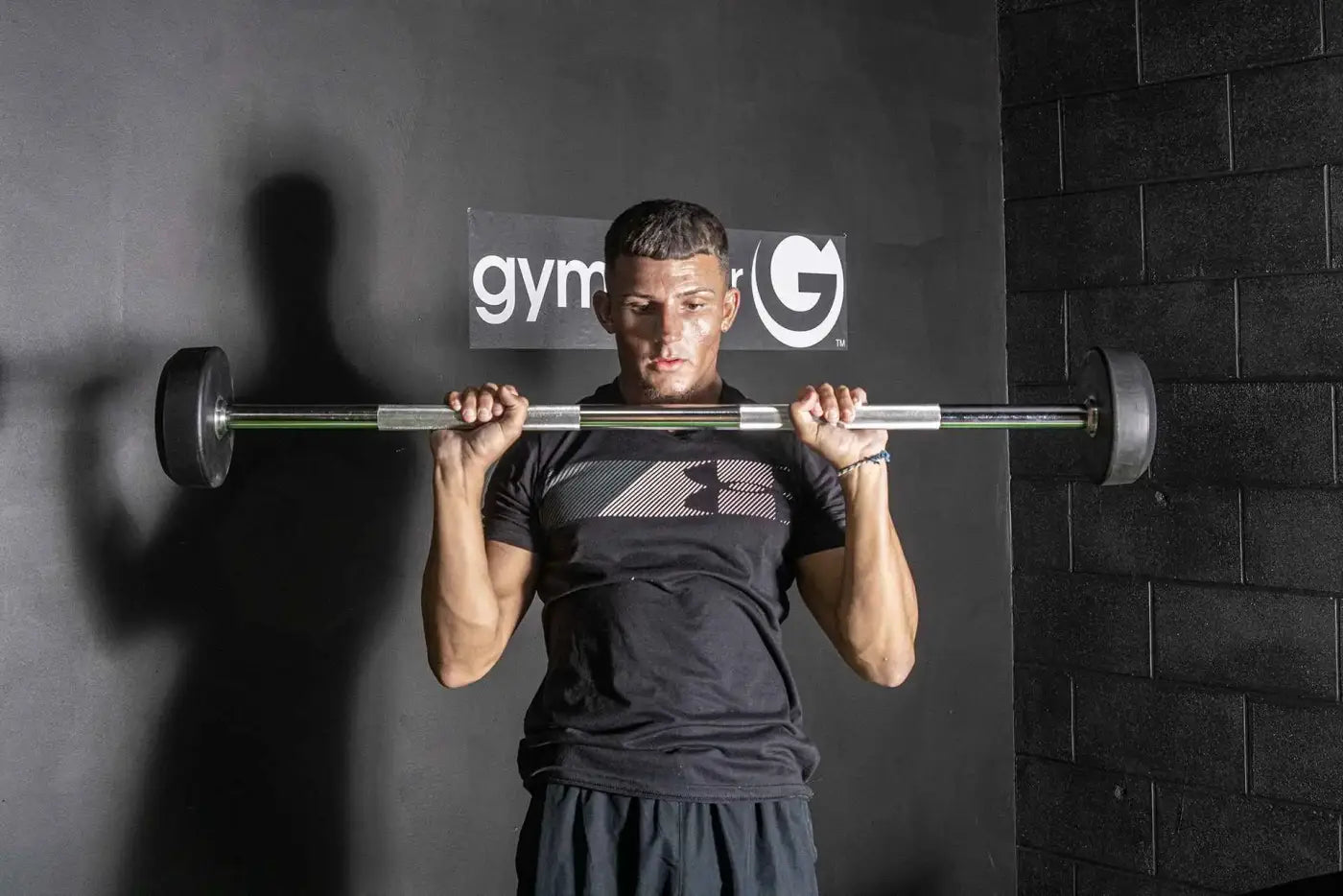 A man holding a silver fixed rubber barbell with black weight plates for strength training uk delivery available