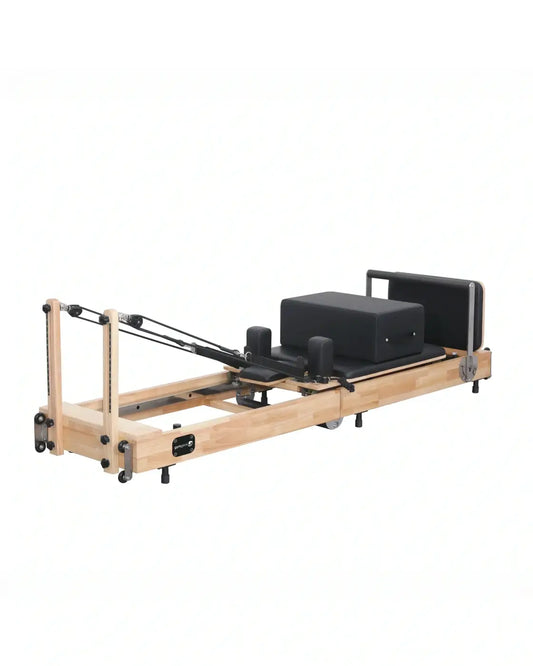 A sleek foldable reformer pilates machine in light oak wood with black padded surfaces and adjustable resistance cables