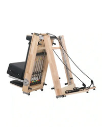 Light-colored oak foldable pilates reformer with black padded seat, adjustable resistance bands, and metal pulleys uk delivery