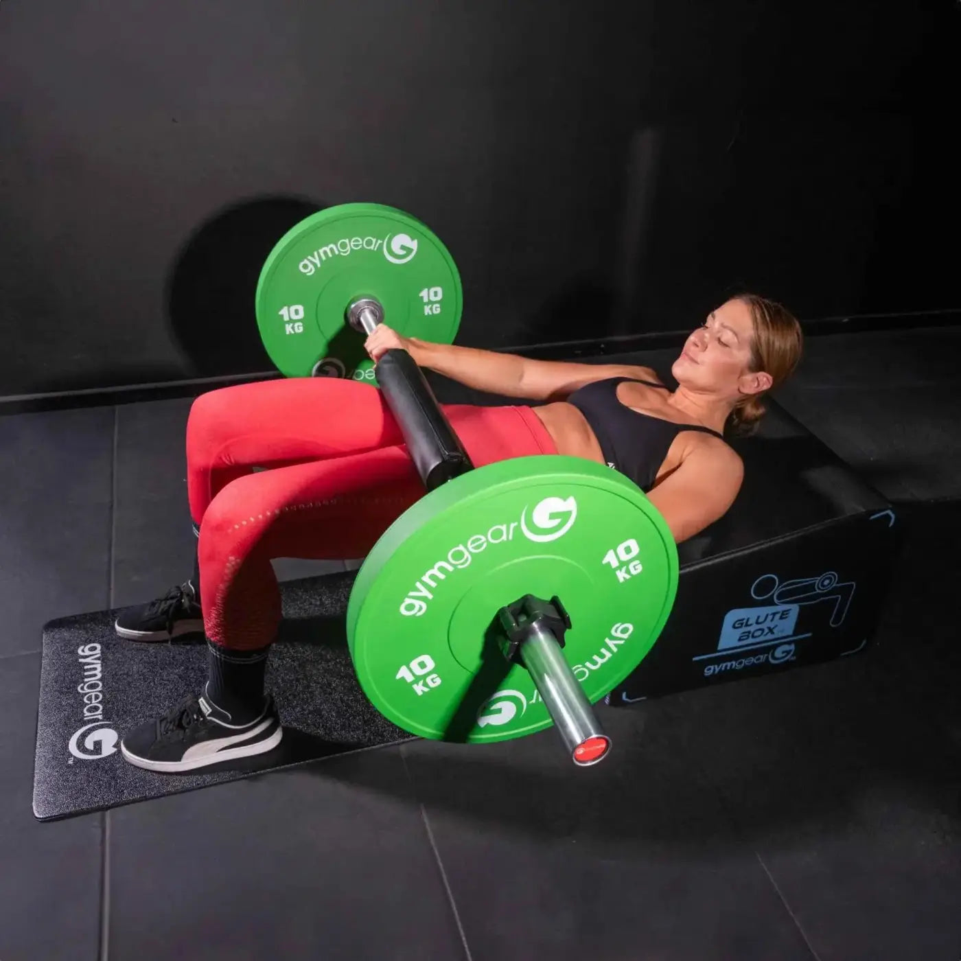 Green 10 kg gymgear weight plates on a barbell for strength training with gym gear angled glute box home workout