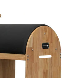 Light wood-finished gym gear ladder barrel with black padded surface and logo plaque designed for space-saving Pilates