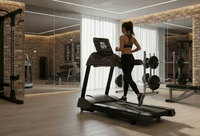 A woman in athletic wear runs on a treadmill inside a modern gym with brick walls, mirrors, weight racks, and motivational wall art.
