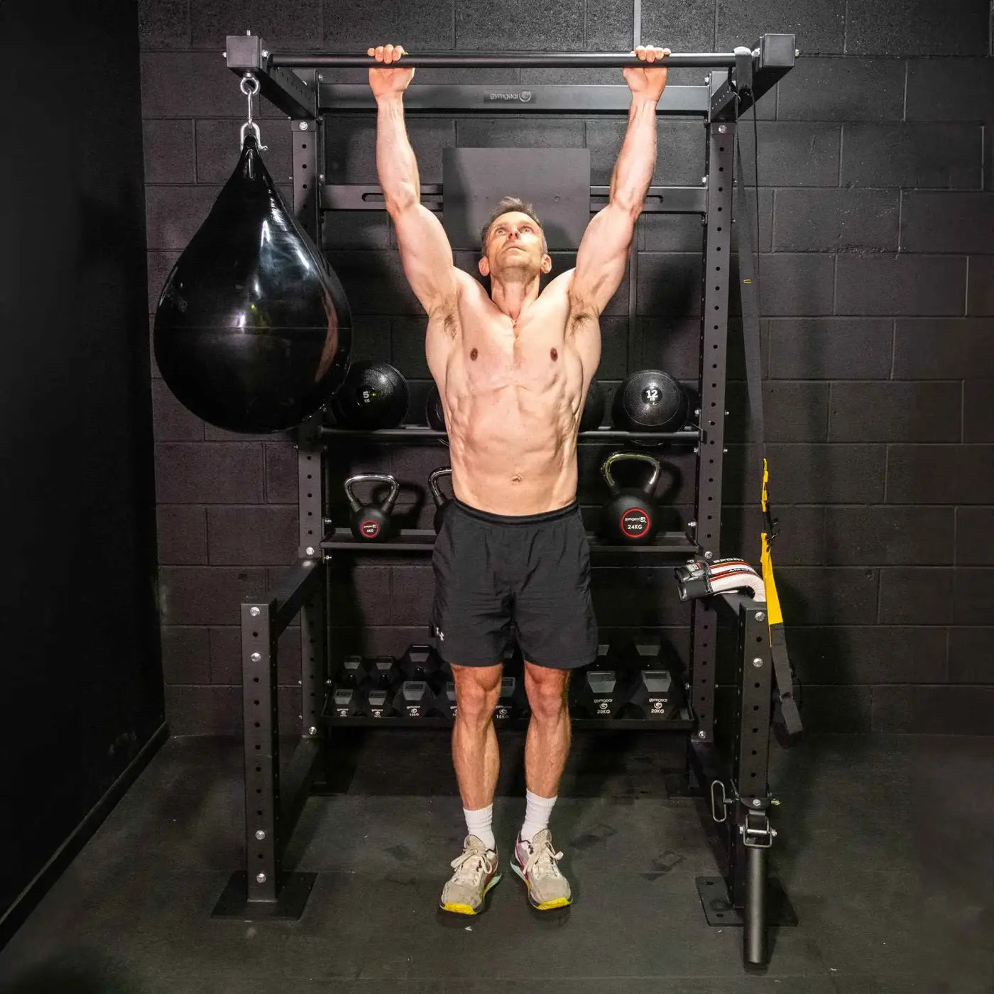 A muscular man performing a pull-up on a black metal HIITMax training station for home gyms
