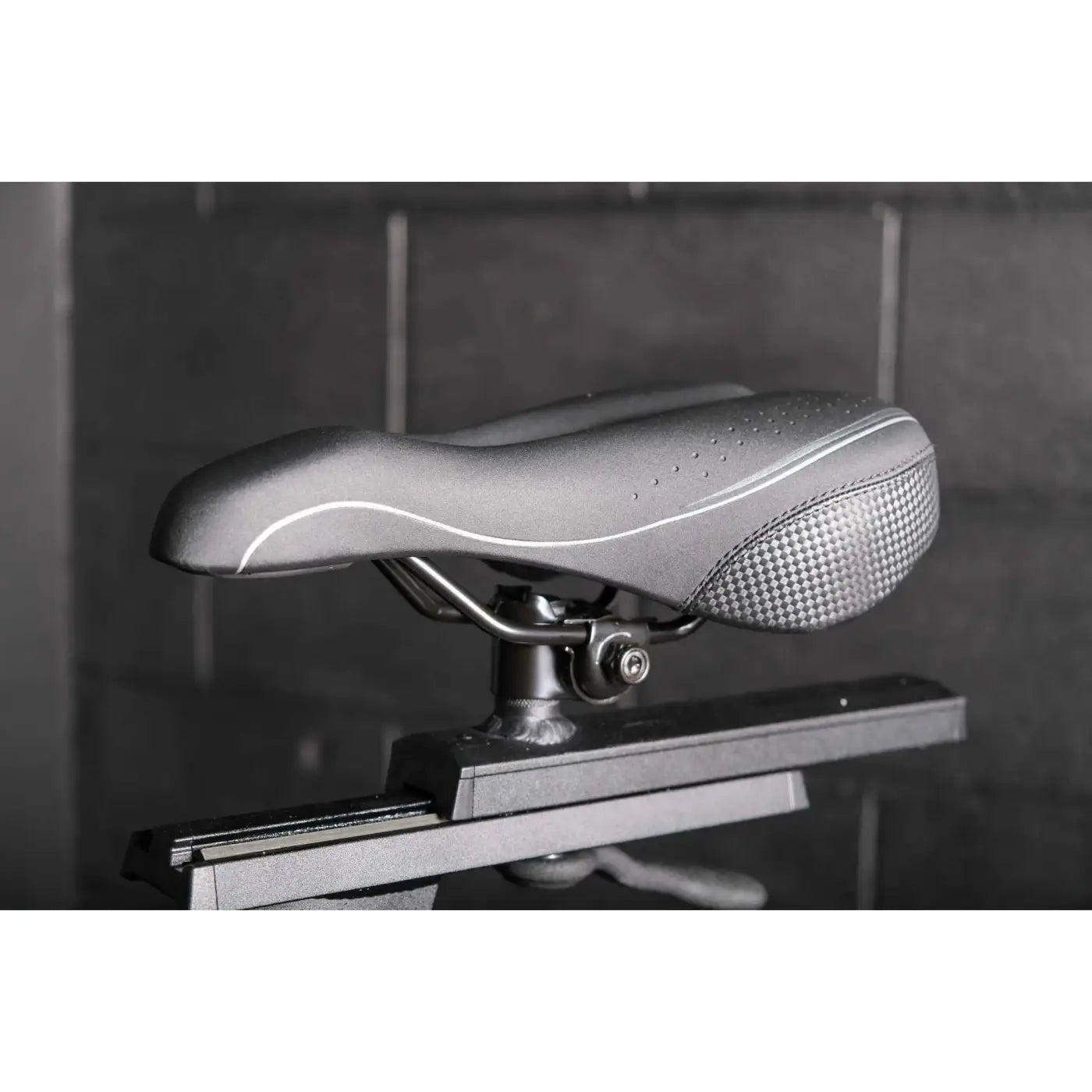 Silver textured perforated bicycle saddle with white stitching on the m sport elite upright exercise bike uk model